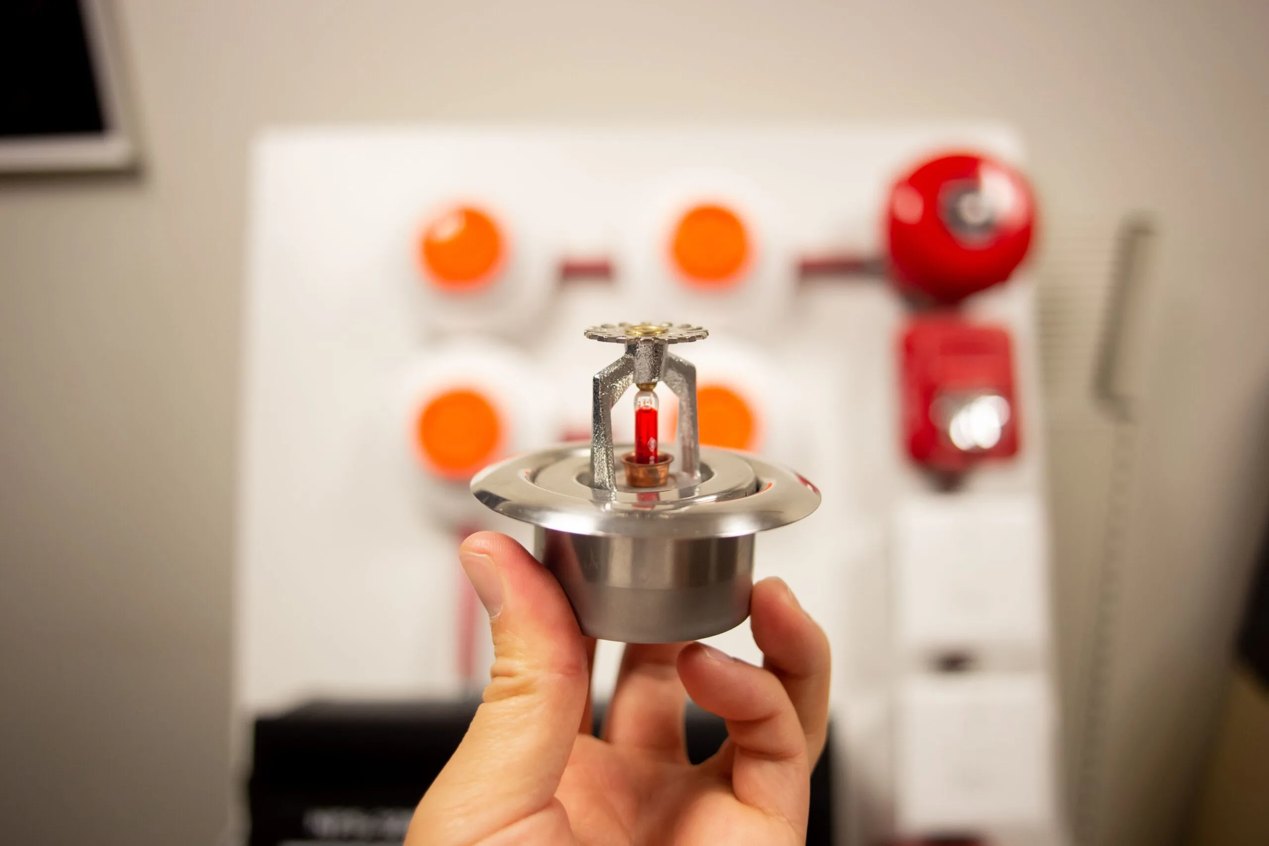 A hand holding a silver fire alarm system sensor