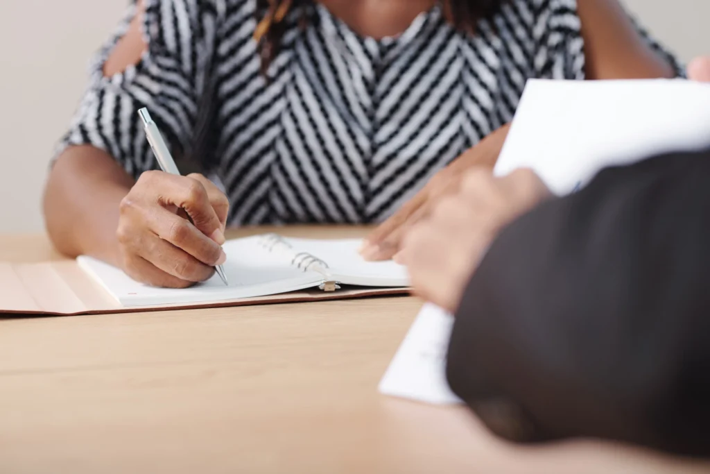 Businesswoman taking notes in planner while listening to coworker at meeting