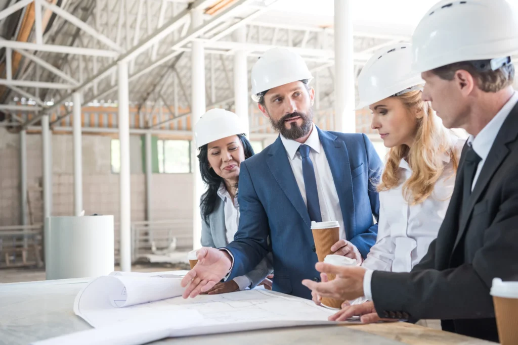 group of contractors in formal wear talking while working with blueprints at construction