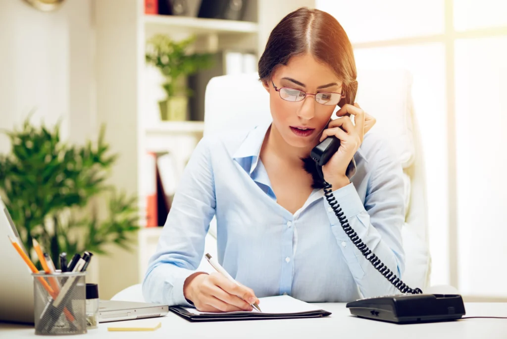 Woman working at her desk in the office. She is using phone and checking references.